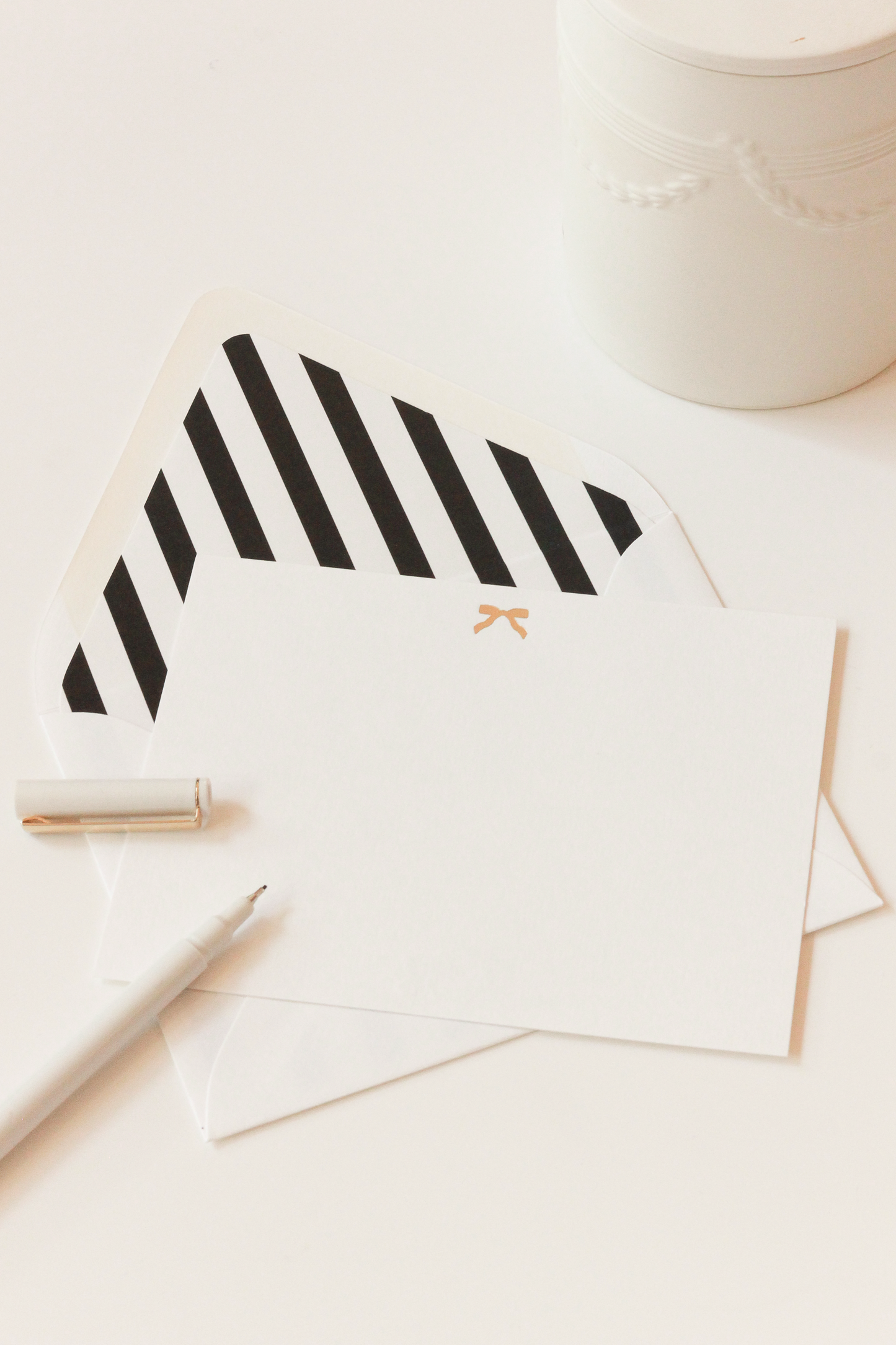 White envelope with black and white stripes and a notecard with a gold bow on a white background