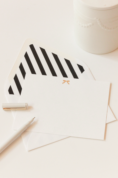 White envelope with black and white stripes and a notecard with a gold bow on a white background